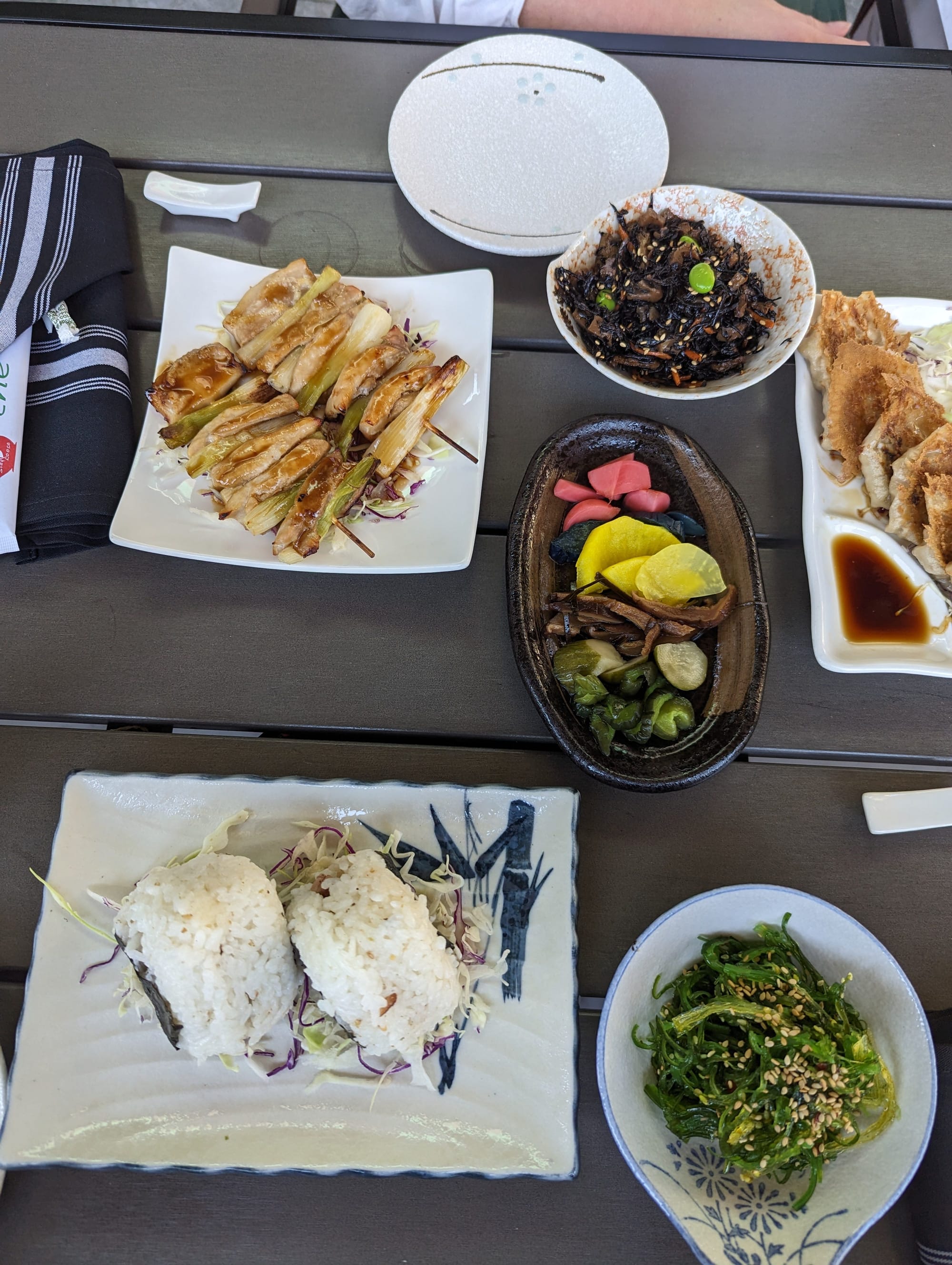 A photo of several square plates and small rounded platters on which a multitude of multicolored Japanese appetizers has been served. 