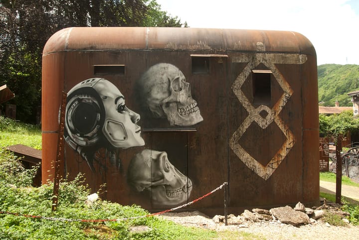 Graffiti on a rusted metal structure featuring a robot, skulls, and geometric shapes.